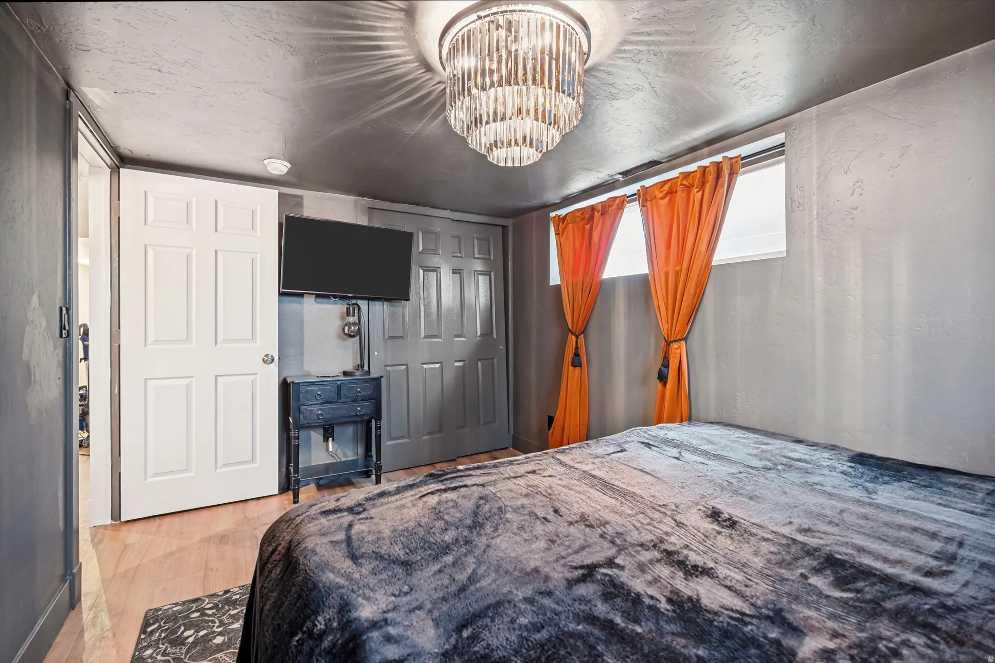 Room featuring a crystal chandelier, wood-finish flooring, and a wall-mounted television