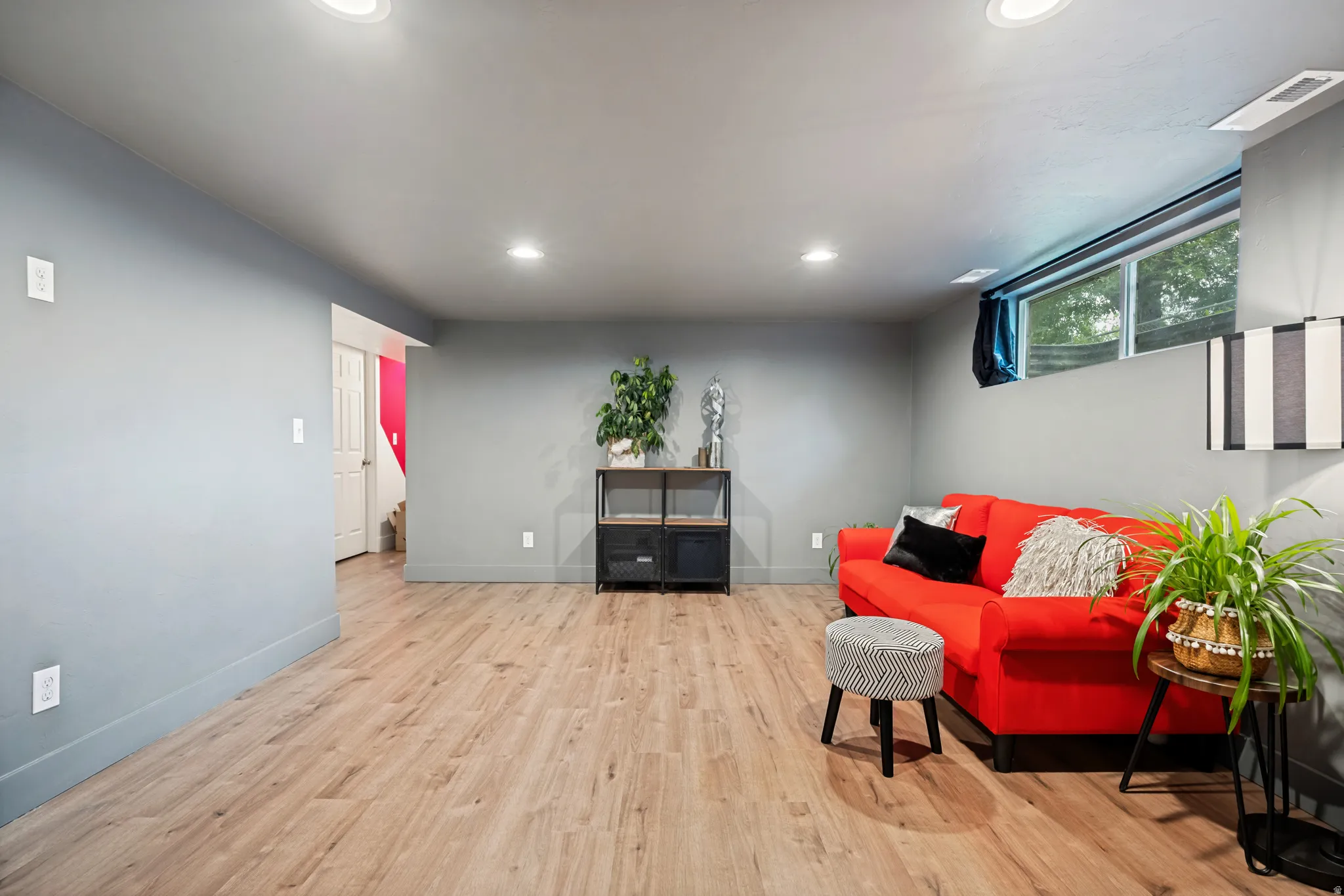 Spacious lower-level room featuring light wood-finish flooring, recessed lighting, and a large egress window