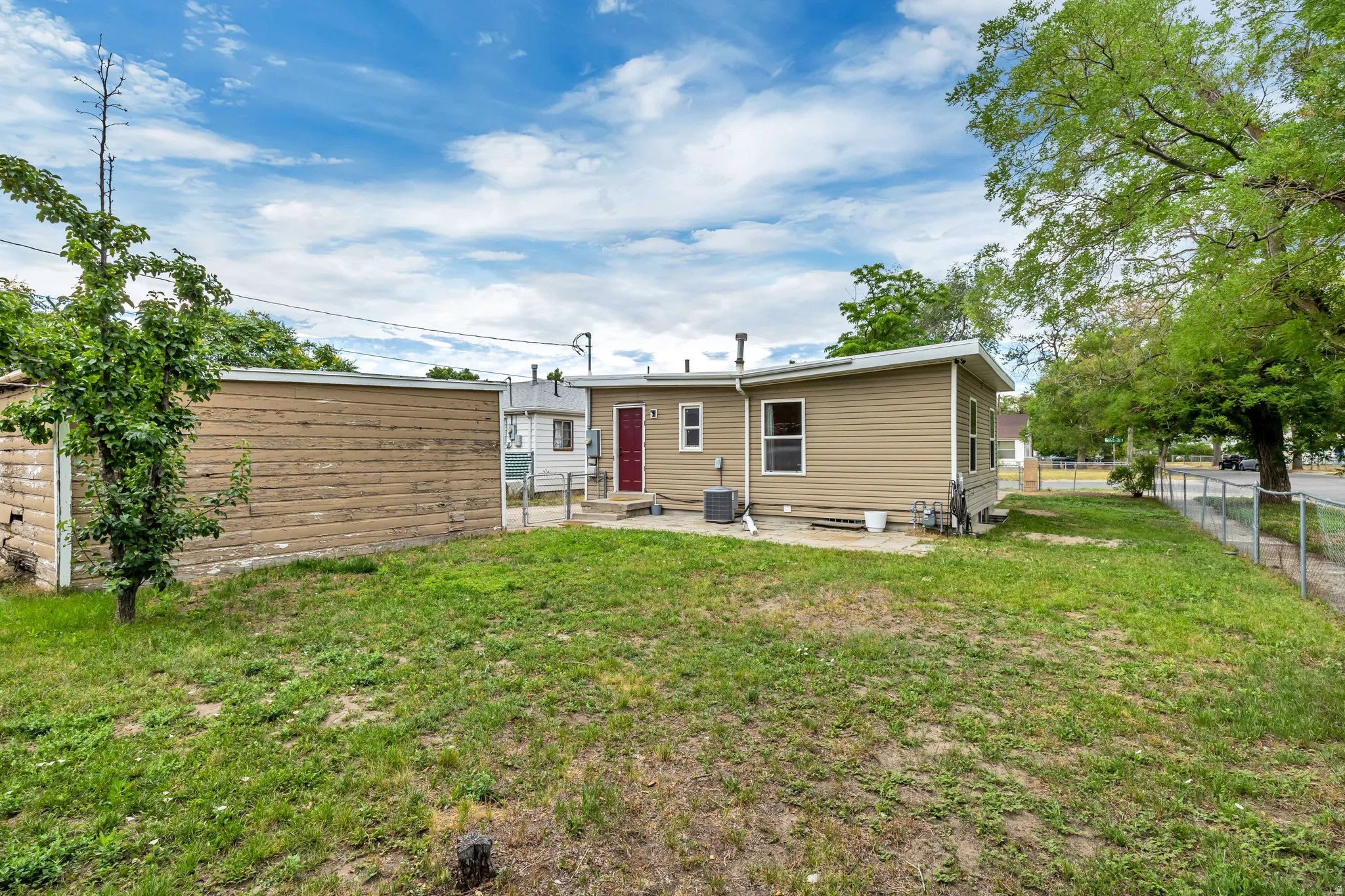 Rear exterior featuring tan horizontal siding, a red entry door, a chain-link fence, and a grass lawn