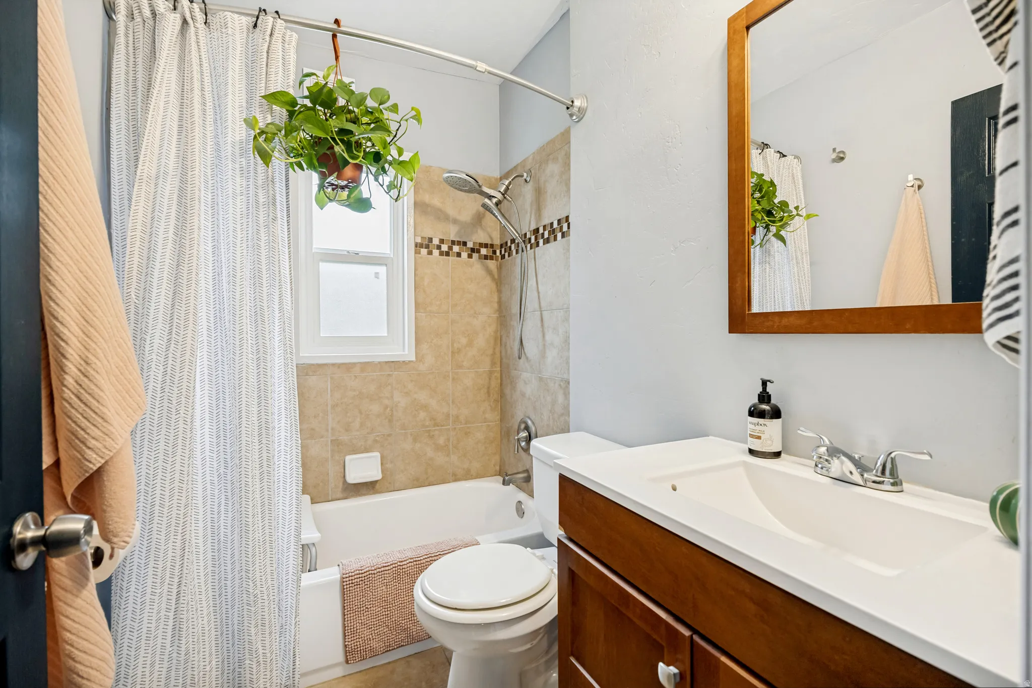 Bathroom featuring a wood-finish vanity with an integrated sink, a rectangular mirror, and a tiled shower/tub combination with an accent border
