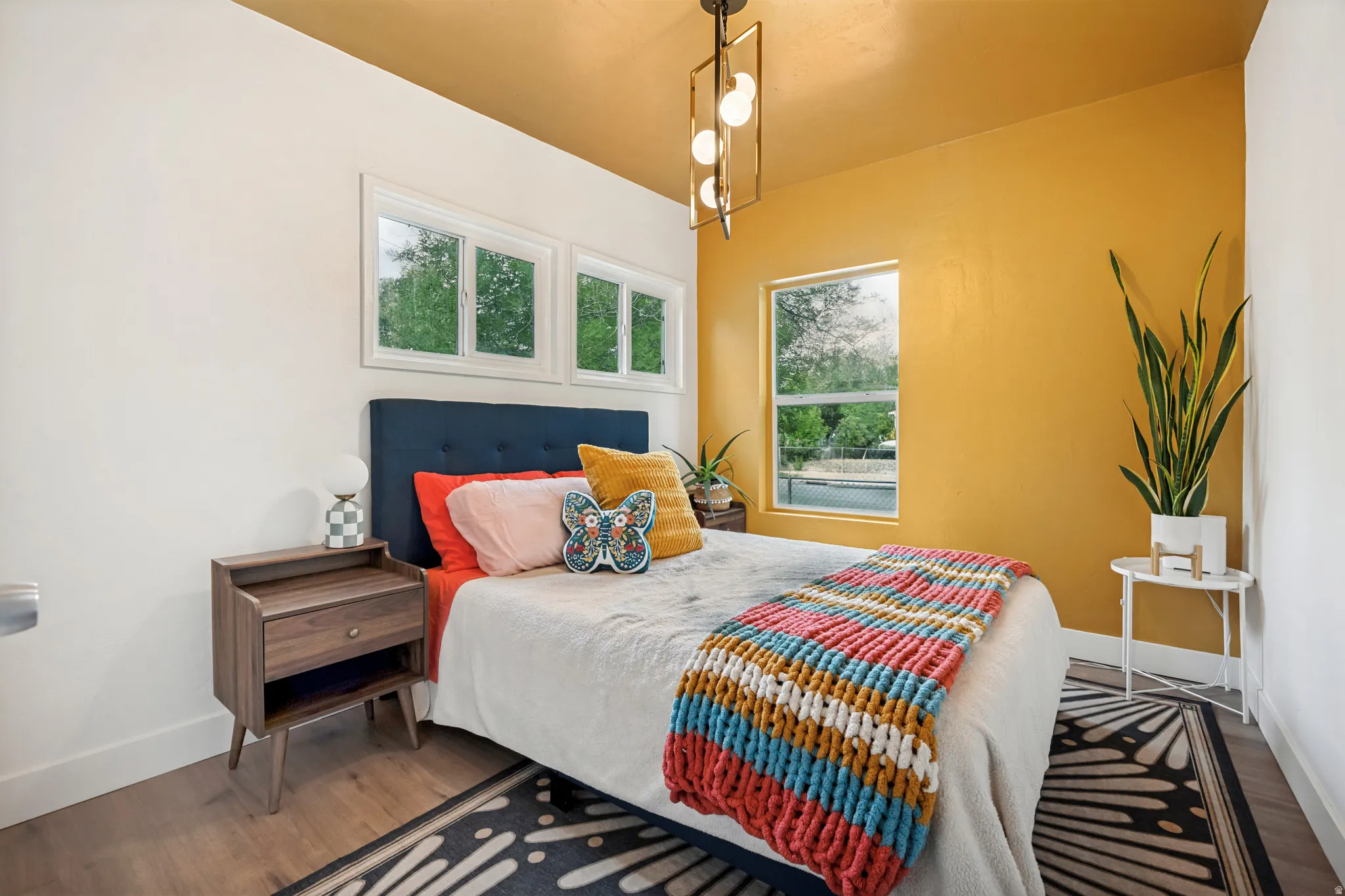 Bedroom featuring a vibrant accent wall, wood-finish flooring, a contemporary ceiling light fixture, and multiple windows providing natural light