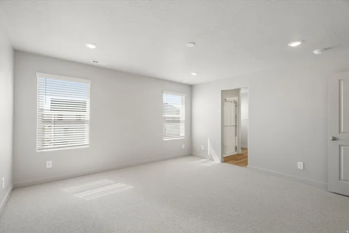 **DISCLAIMER** Interior package may vary. Carpeted room featuring recessed lighting, two windows with blinds, a white paneled door, and an open doorway revealing a bathroom with a glass shower enclosure and wood-finish flooring