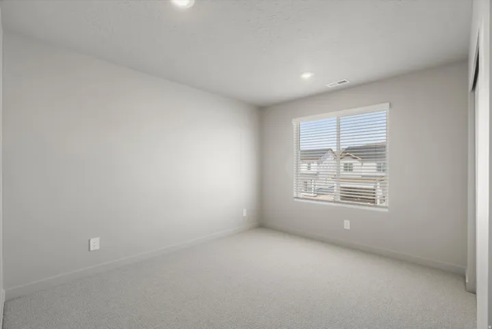 **DISCLAIMER** Interior package may vary. Neutral-toned room featuring a large window with blinds, recessed lighting, and light gray wall-to-wall carpeting