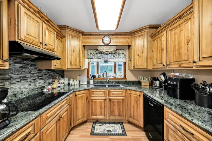 U-shaped kitchen featuring wood cabinetry, dark green stone countertops, a mosaic tile backsplash, built-in cooktop, and a double basin sink with a window