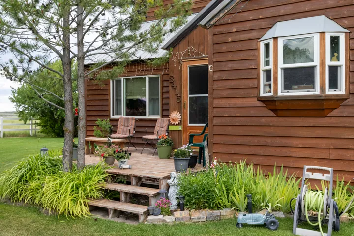 Wood-sided exterior featuring a front entry deck with three steps, an octagonal bay window, and mature landscaping