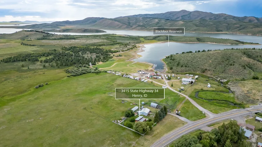 Aerial perspective featuring expansive green fields, a substantial body of water, and surrounding mountains