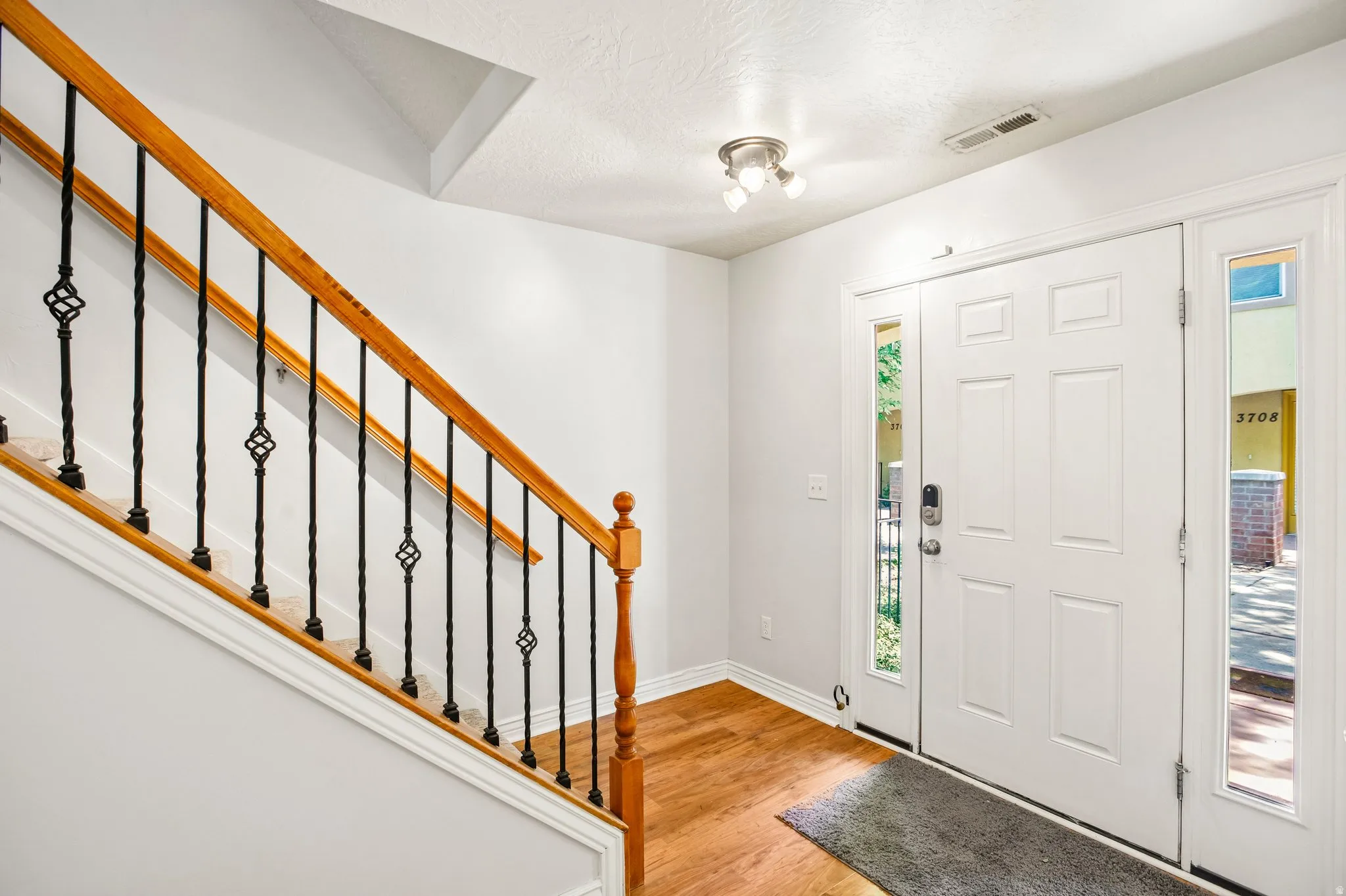 Entryway featuring wood-finish flooring, a white paneled door with sidelight windows, and a staircase with wood handrails and decorative wrought iron balusters