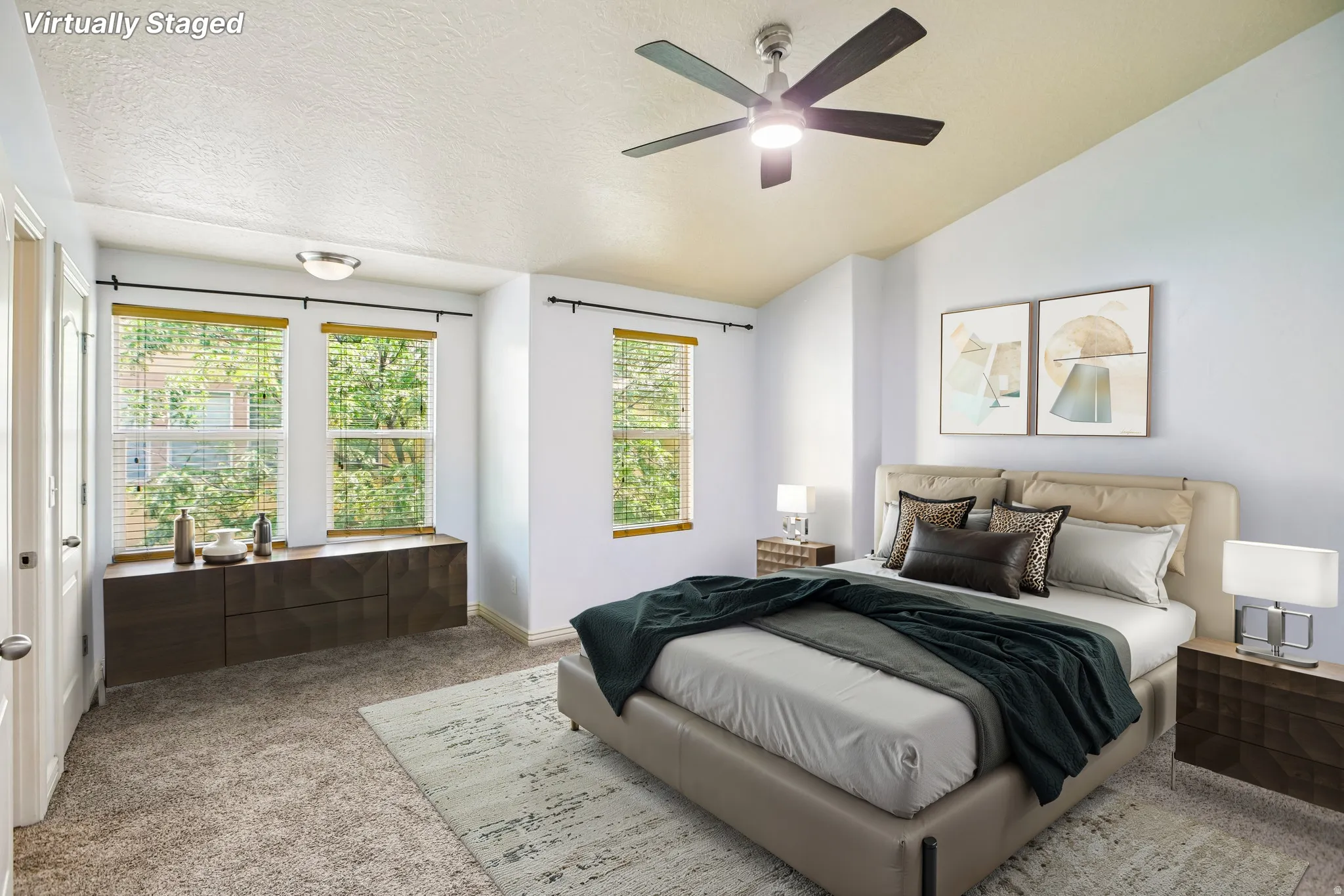 Spacious bedroom featuring carpet flooring, multiple windows with blinds, a built-in window seat with storage, a ceiling fan with integrated lighting, and a light-colored wall finish