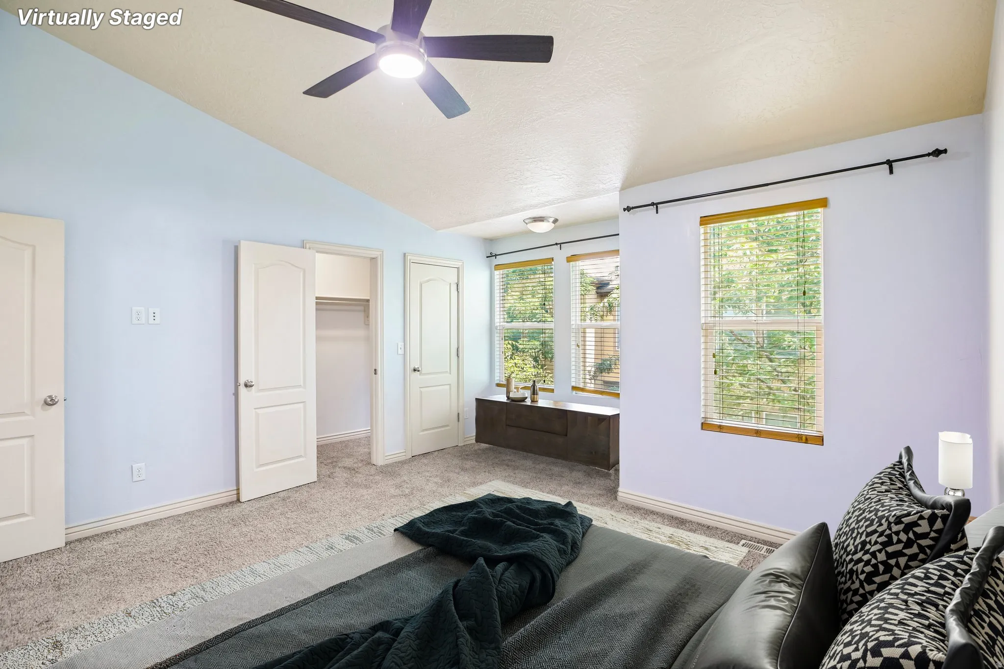 Spacious room featuring vaulted ceilings with a ceiling fan, plush carpeting, multiple windows with blinds, and ample closet space