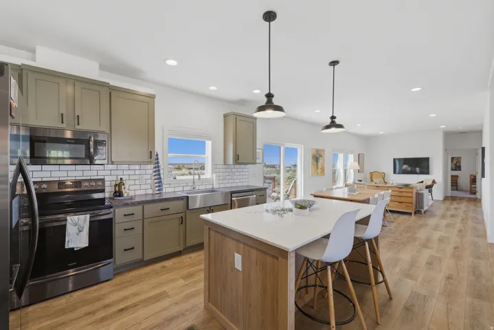 Open-concept kitchen featuring olive-toned cabinetry with matte black hardware, stainless steel appliances, and a farmhouse sink