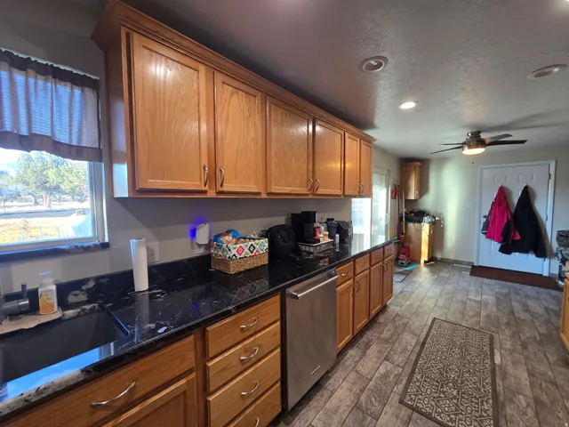 Kitchen featuring wood cabinetry, dark countertops, and stainless steel dishwasher