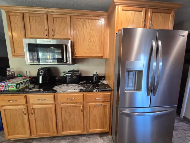 Kitchen featuring natural wood cabinetry, dark countertops, an integrated stainless steel microwave, and a stainless steel French door refrigerator