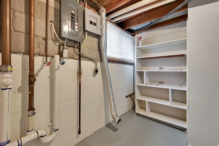 Utility area featuring exposed copper and PVC plumbing, an electrical panel, and built-in shelving