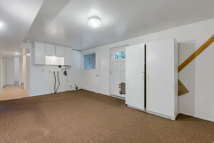 Carpeted room with a built-in laundry area featuring upper cabinetry and wall connections for appliances