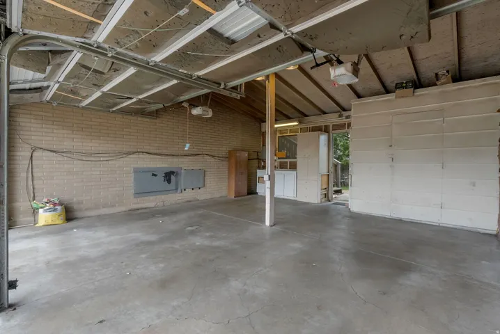 Spacious carport featuring a concrete floor, exposed wood beam ceiling, and a brick accent wall