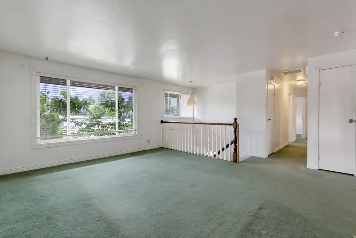Spacious room featuring multiple windows, a wood and white spindle railing, and a hallway with flush-mount lighting fixtures
