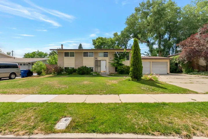 Split-level residence featuring a two-car garage, mature front yard landscaping, and a concrete driveway