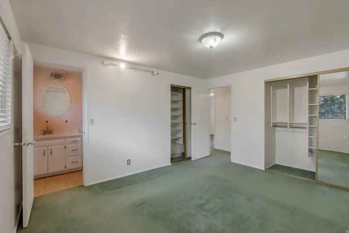 Bedroom with green carpet flooring, featuring a built-in closet with mirrored sliding doors and integrated shelving