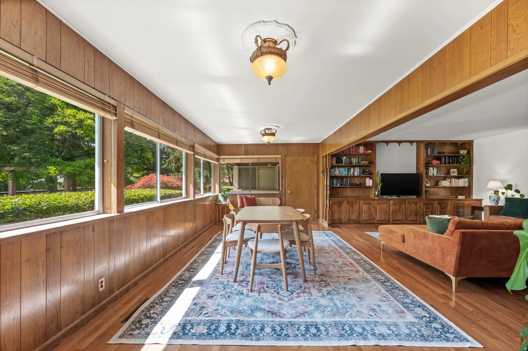 Integrated living and dining areas featuring wood-finish paneling, hardwood flooring, and expansive windows