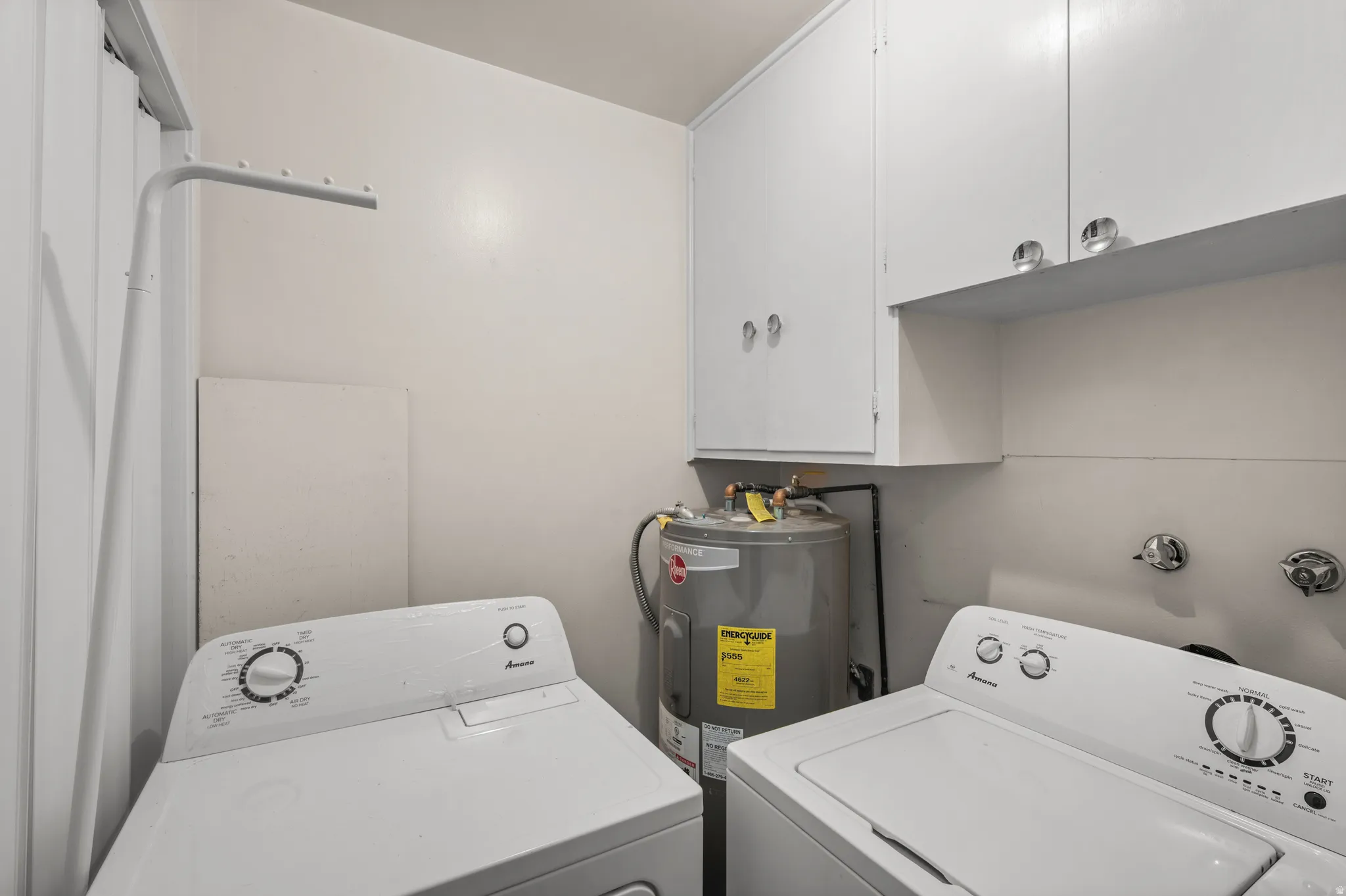 Dedicated laundry area featuring a water heater, upper cabinetry, and a wall-mounted drying rack