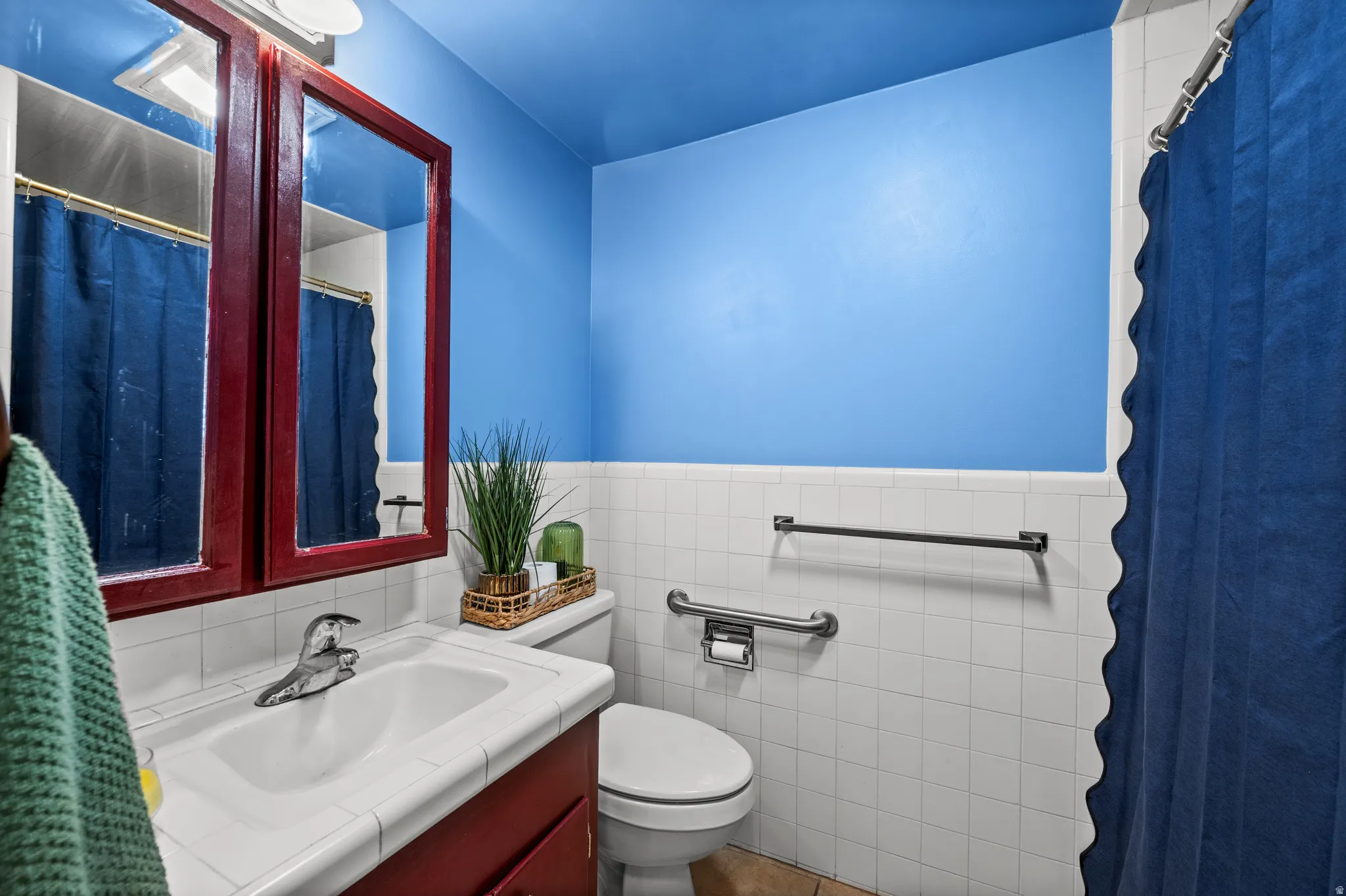 Bathroom featuring a vanity with a white countertop and integrated sink, a dark wood-finish medicine cabinet with mirrored doors, and white square wall tiles