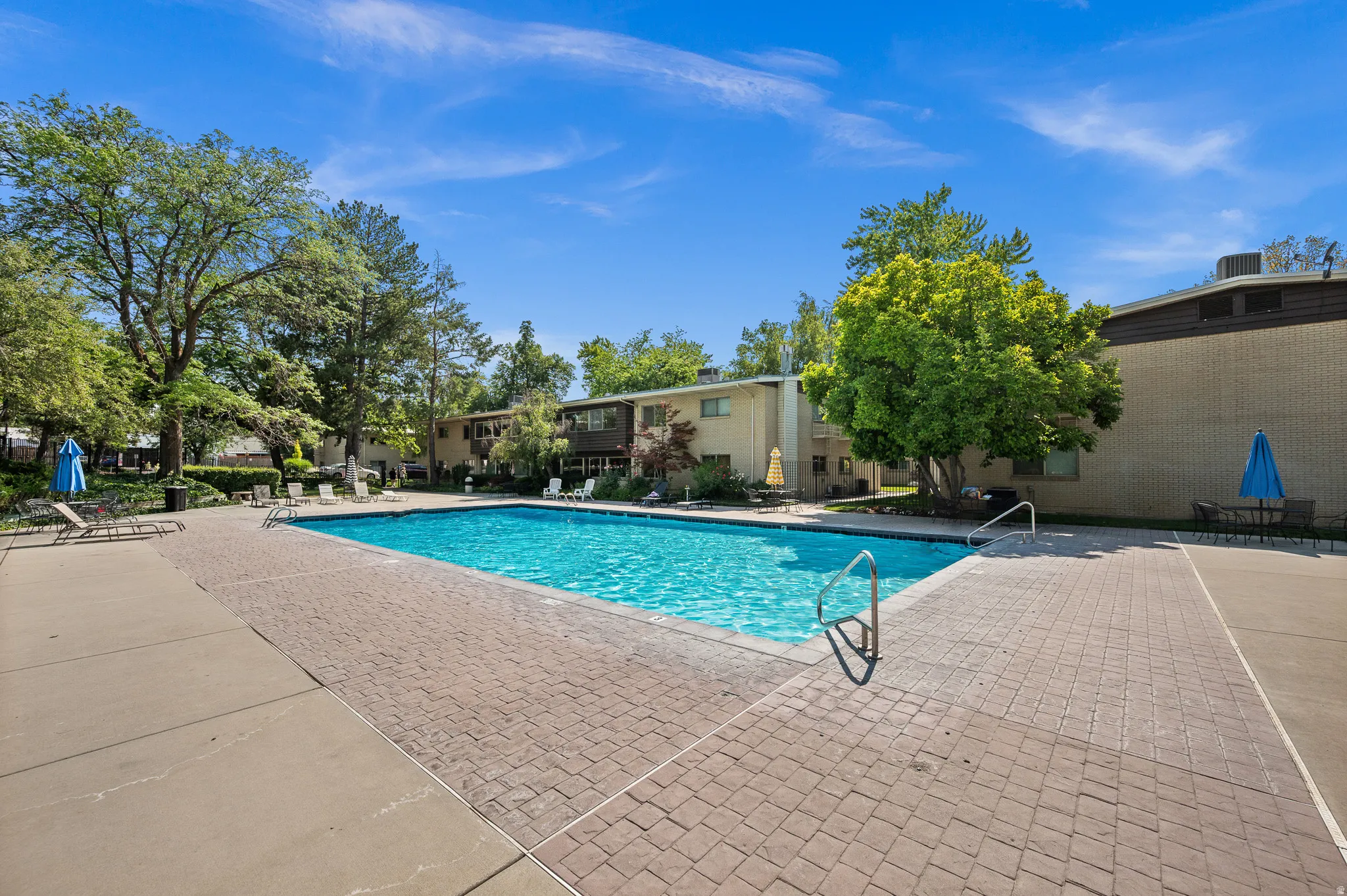 Rectangular swimming pool surrounded by a brick paver deck and concrete walkways