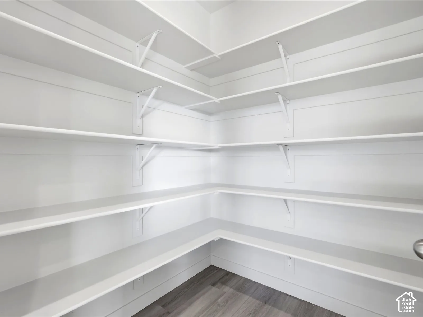 Walk-in storage space featuring custom wrap-around wood shelving, reinforced white metal brackets, and wood-finish flooring