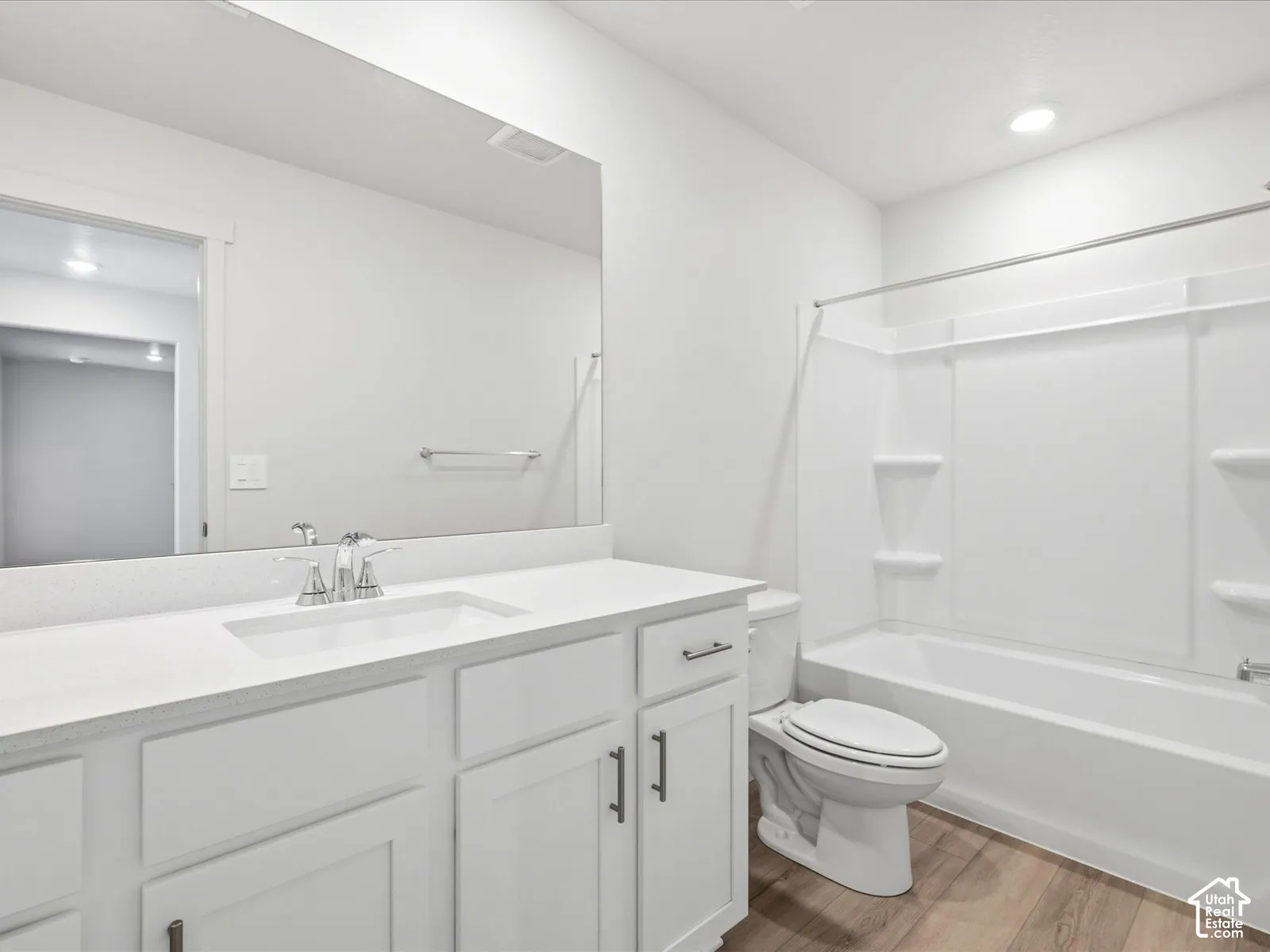 Bathroom featuring white cabinetry, solid-surface countertop with integrated sink, full-width wall mirror, wood-finish flooring, and a tub-shower combination with built-in shelving