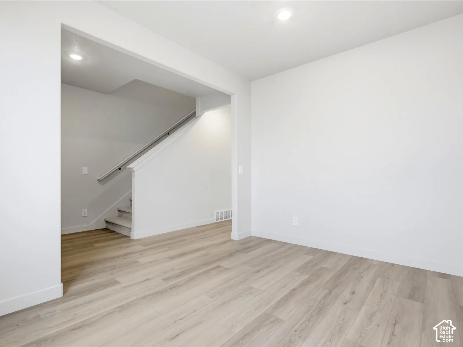 Neutral wall palette with wood-finish flooring, recessed lighting, and a staircase featuring a metal handrail