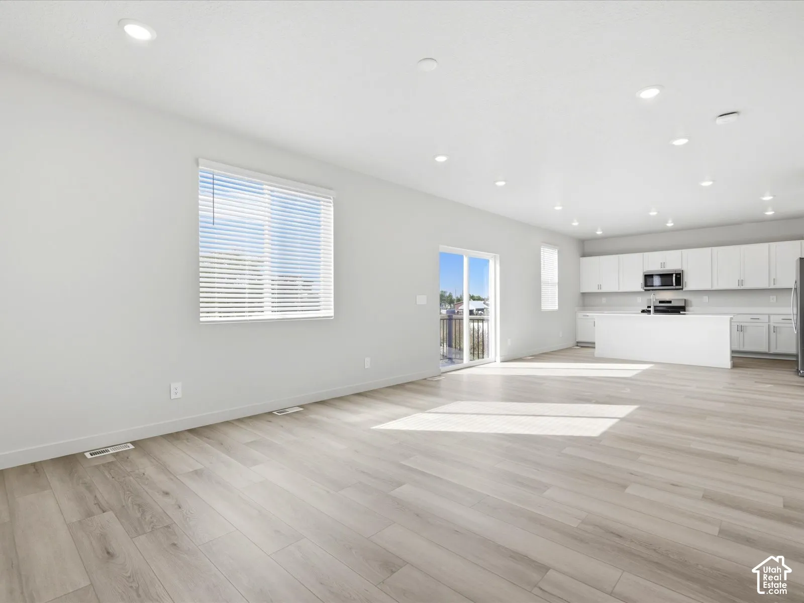 Open-concept area featuring wood-finish flooring, recessed lighting, white cabinetry, a central kitchen island, and a sliding glass door