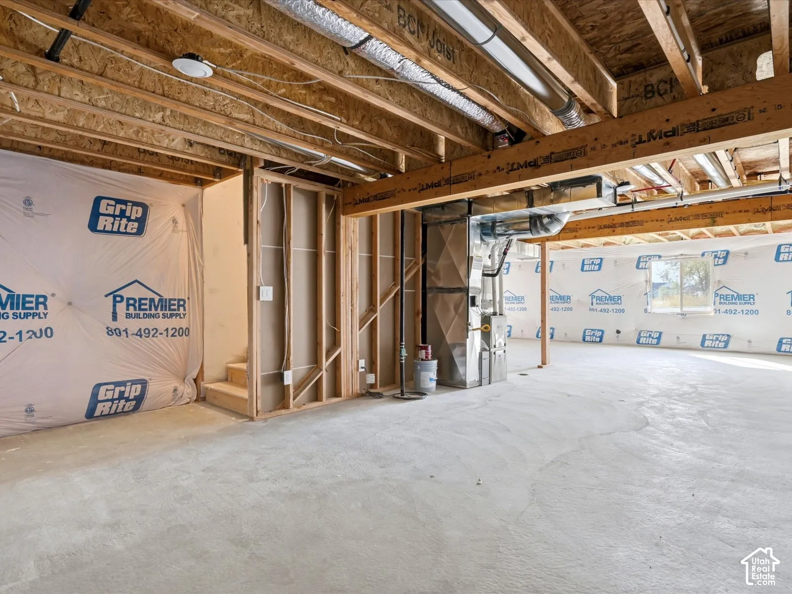 Unfinished lower level featuring exposed wood joist ceilings, concrete flooring, stud-frame walls with vapor barrier sheeting, and a central HVAC system