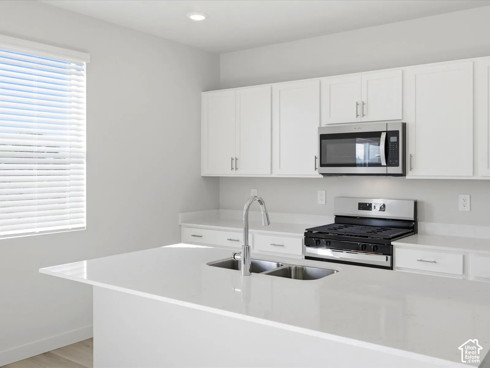 Kitchen featuring white shaker-style cabinetry, quartz countertops, a central island with a double-basin stainless steel sink, a gooseneck faucet, and stainless steel appliances including an over-the-range microwave and gas range