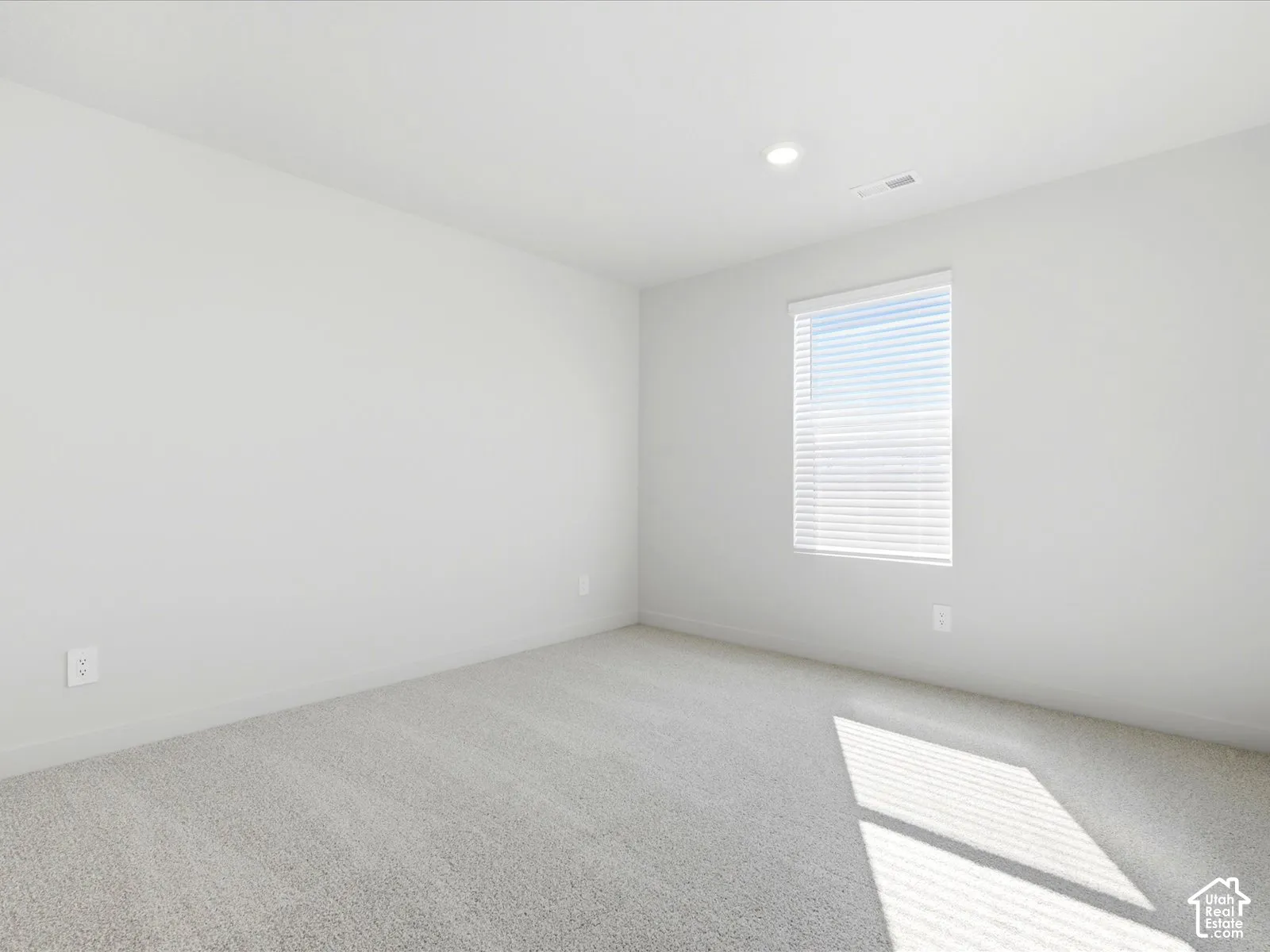 Neutral-toned carpeting, crisp white walls, recessed ceiling lighting, and a single window with horizontal blinds