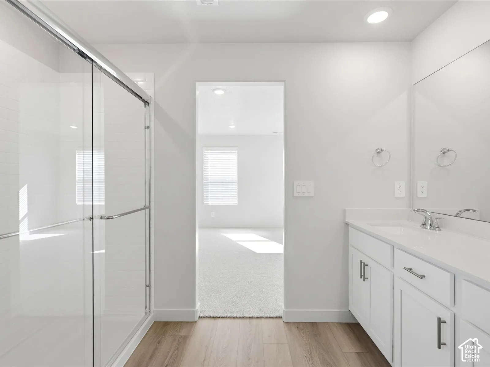 Bathroom featuring a walk-in glass-enclosed shower, white vanity cabinet with a solid-surface countertop, full-width vanity mirror, and wood-finish flooring