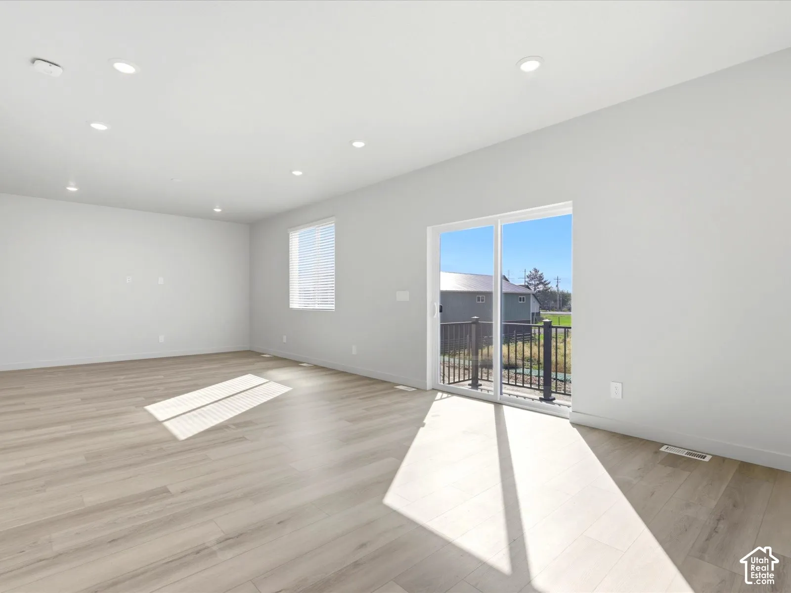 Open-concept space featuring wood-finish flooring, recessed lighting, neutral wall tones, and glass sliding doors leading to an exterior balcony