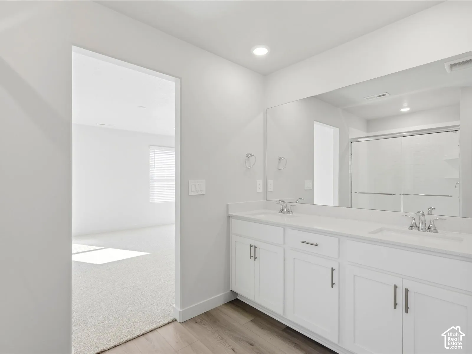 Double vanity featuring white cabinetry, solid-surface countertop, dual integrated sinks, polished chrome hardware, and full-width vanity mirror