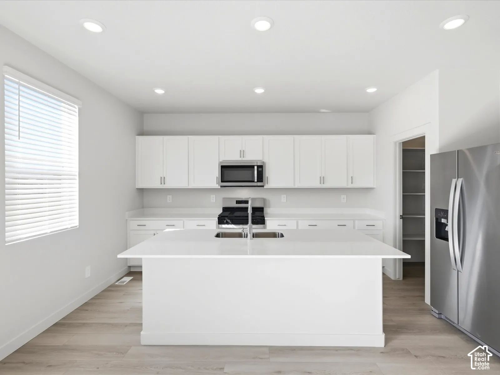 Kitchen featuring a central island with white countertops, white cabinetry, stainless steel appliances, recessed ceiling lighting, and wood-finish flooring