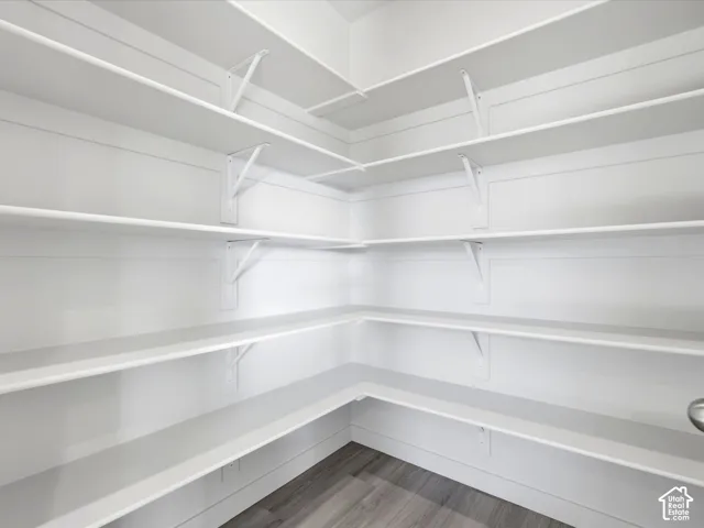 Walk-in storage space featuring custom wrap-around wood shelving, reinforced white metal brackets, and wood-finish flooring