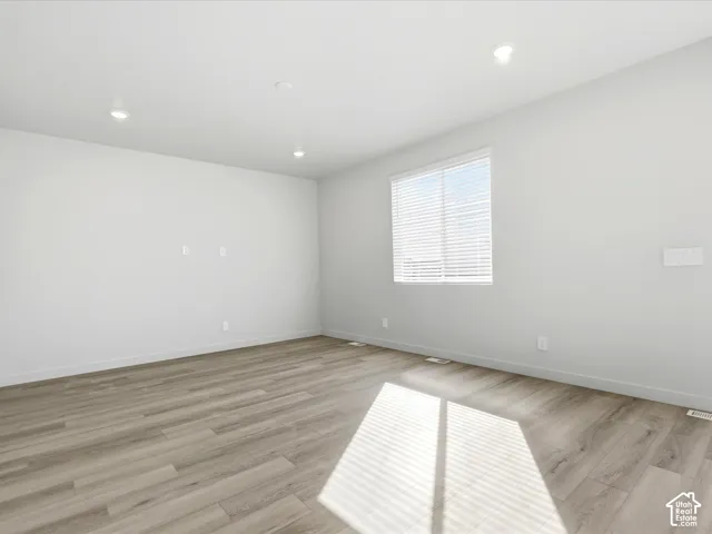Neutral-toned interior space featuring wood-finish flooring, recessed lighting, and a single window with horizontal blinds