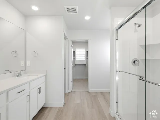 Bathroom featuring wood-finish flooring, white cabinetry with a light-toned countertop, a full-width mirror, recessed lighting, and a glass-enclosed shower