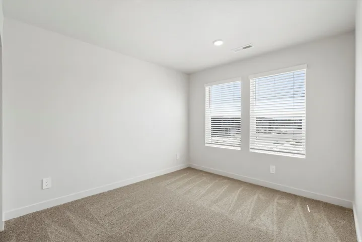 **DISCLAIMER** Interior package may vary. Neutral-toned room featuring a light-colored carpet, white baseboards, and two windows with blinds
