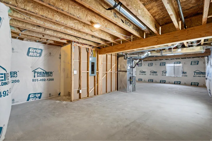 Unfinished basement space featuring exposed wood joists and subflooring, concrete slab, and framed partition walls