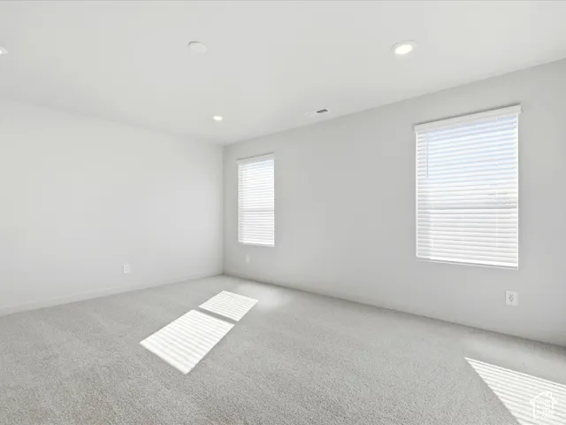 Neutral-toned interior space featuring light wall-to-wall carpeting, recessed ceiling lighting, and dual windows with horizontal blinds