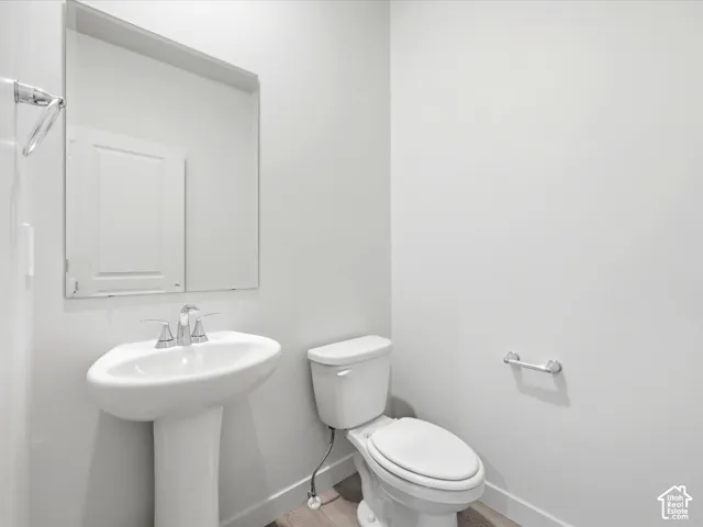 Pedestal sink with a polished chrome faucet, rectangular wall-mounted mirror, white ceramic toilet, and chrome hardware