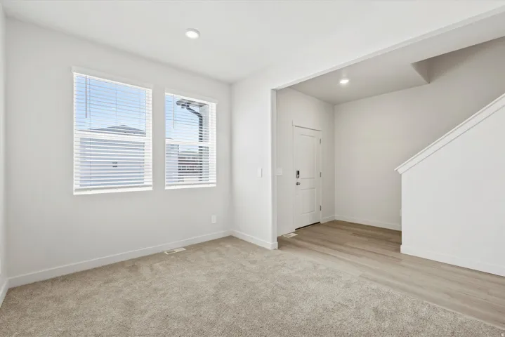 **DISCLAIMER** Interior package may vary. Bright interior space featuring two large windows with blinds, recessed lighting, light-toned wood-finish flooring, and soft carpeting