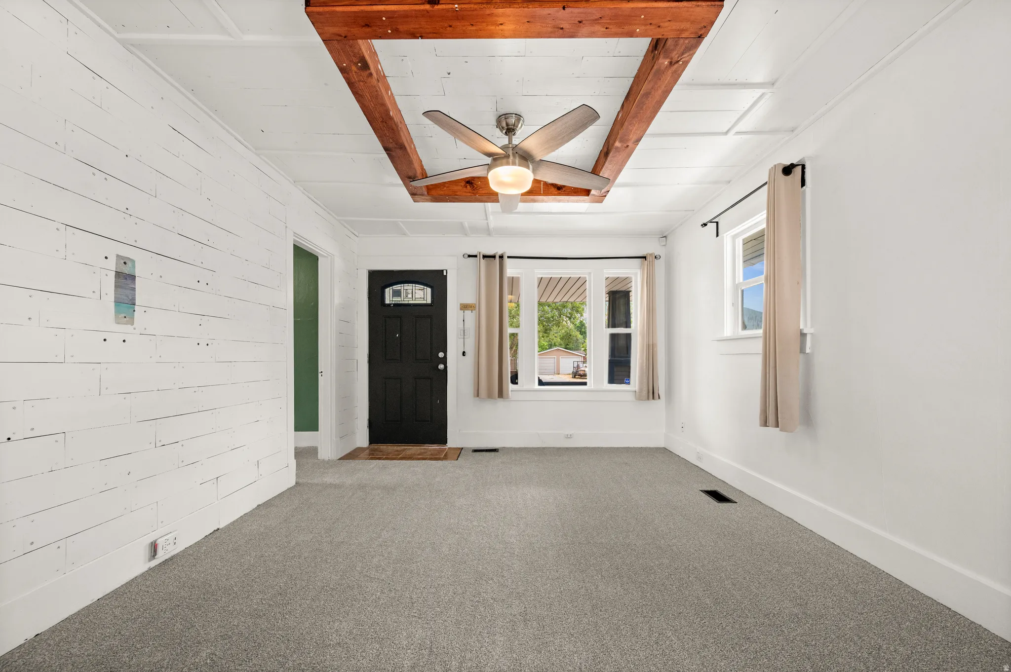 Open-concept living space featuring a wood-beam ceiling accent, a contemporary ceiling fan with integrated lighting, and light gray carpeting