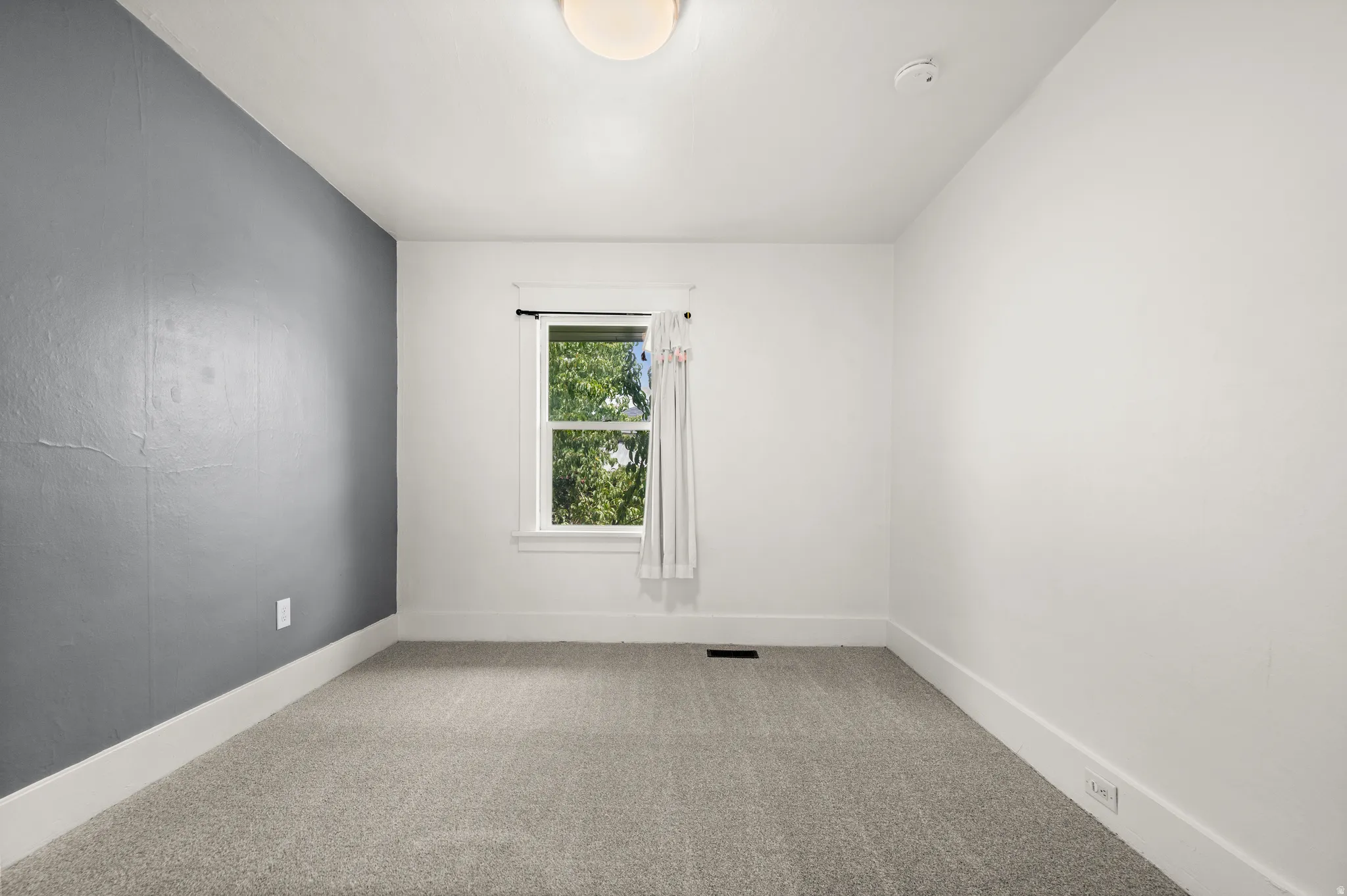 Carpeted room featuring a single window, a contrasting accent wall, white baseboards, and a ceiling-mounted light fixture