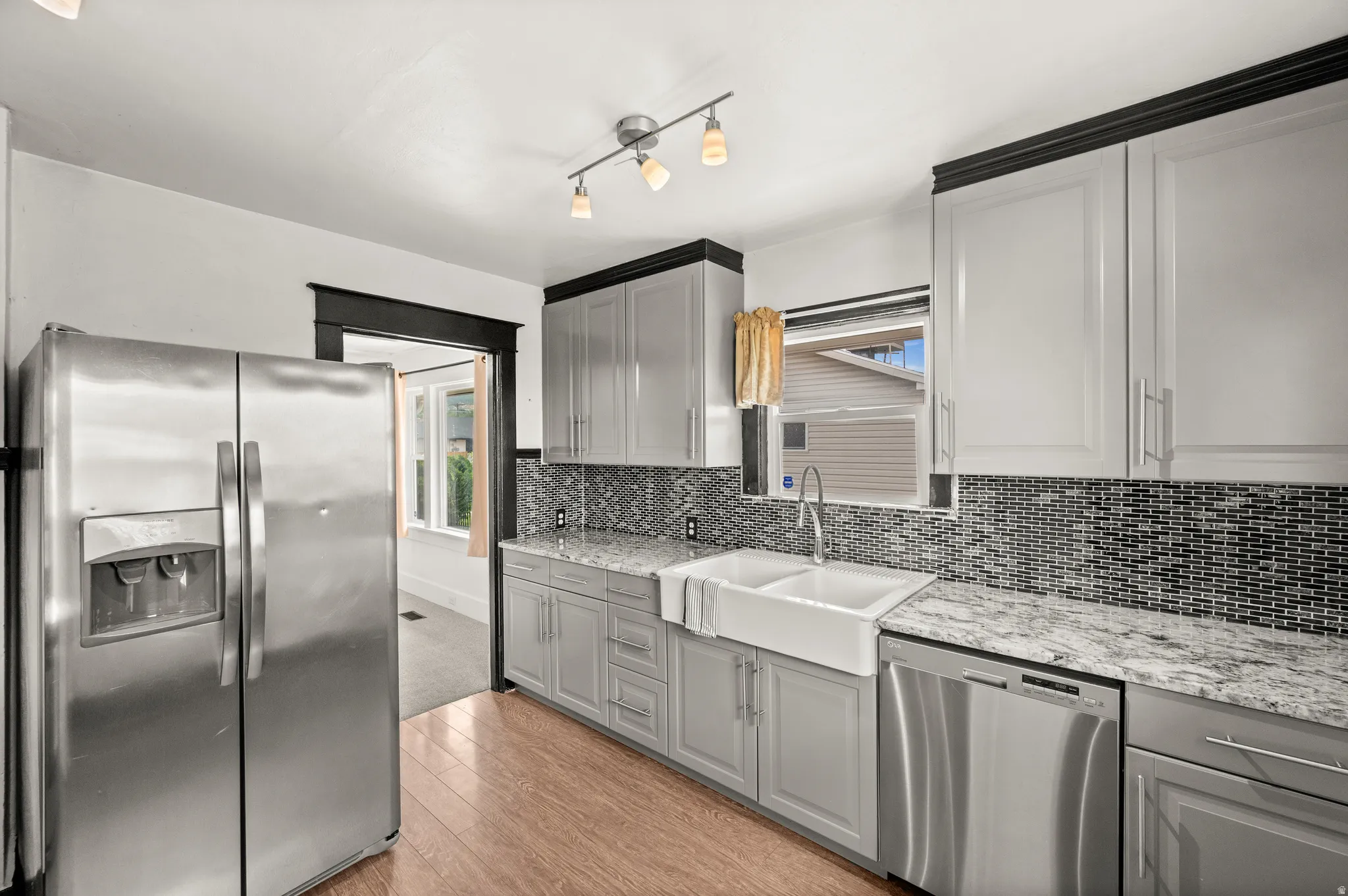 Kitchen featuring light gray cabinetry, a double farmhouse sink, granite-style countertops, mosaic tile backsplash, and wood-finish flooring