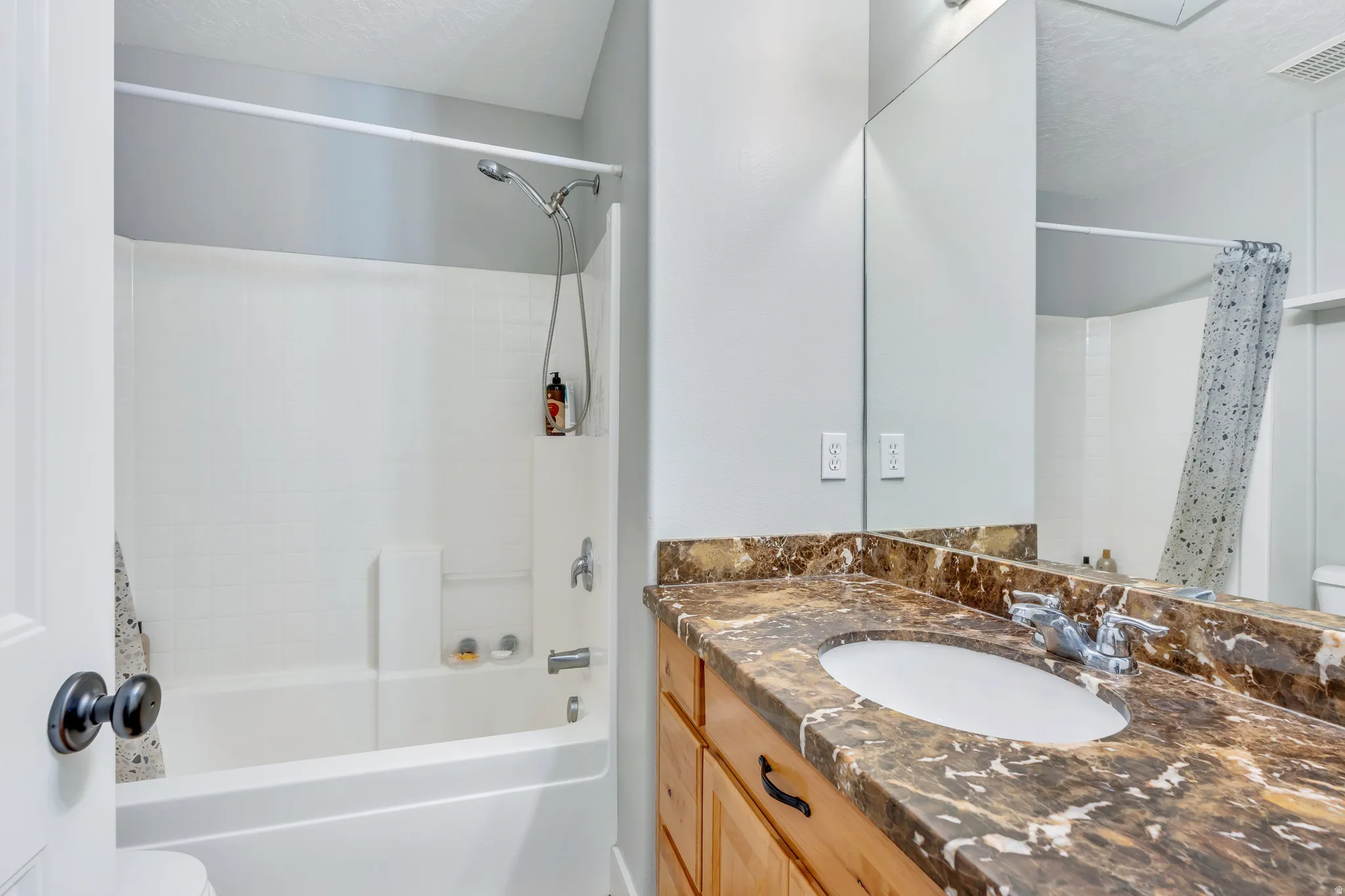 Bathroom featuring a wood-finish vanity with a brown-patterned countertop, an integrated sink, and a chrome faucet
