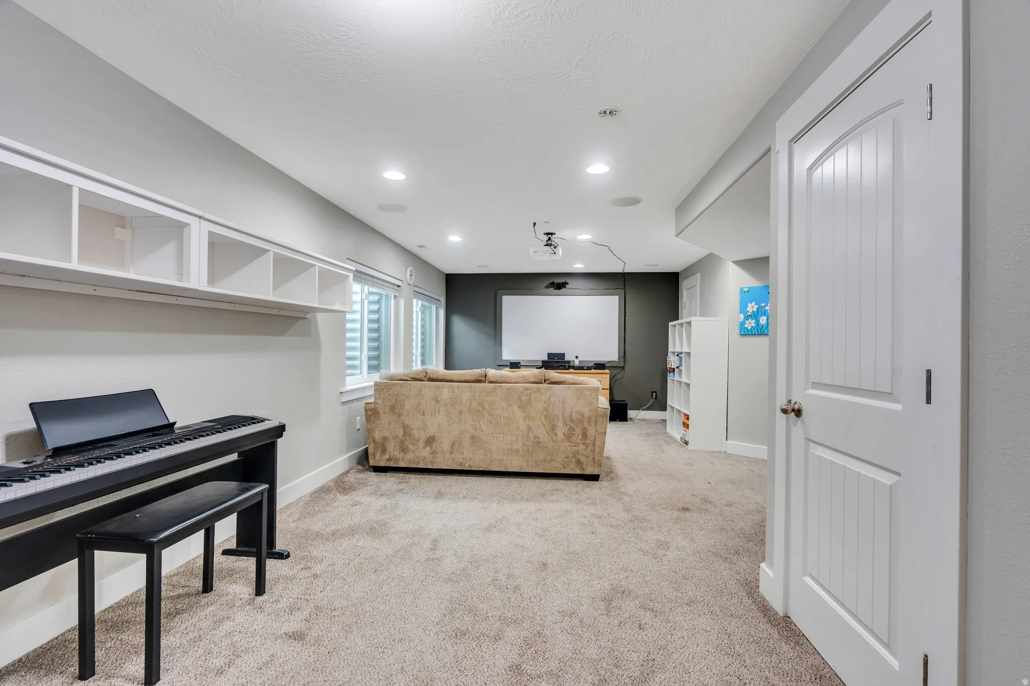 Spacious carpeted room featuring recessed lighting, a built-in wall shelf with open cubbies, and windows with horizontal blinds
